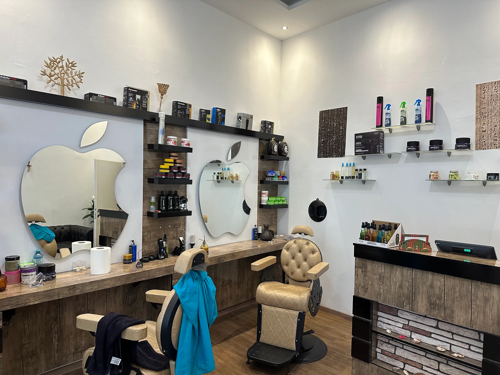 Drei Barberstühle aus beigem Leder vor Spiegeln in Apfelform, Regale mit Pflegeprodukten